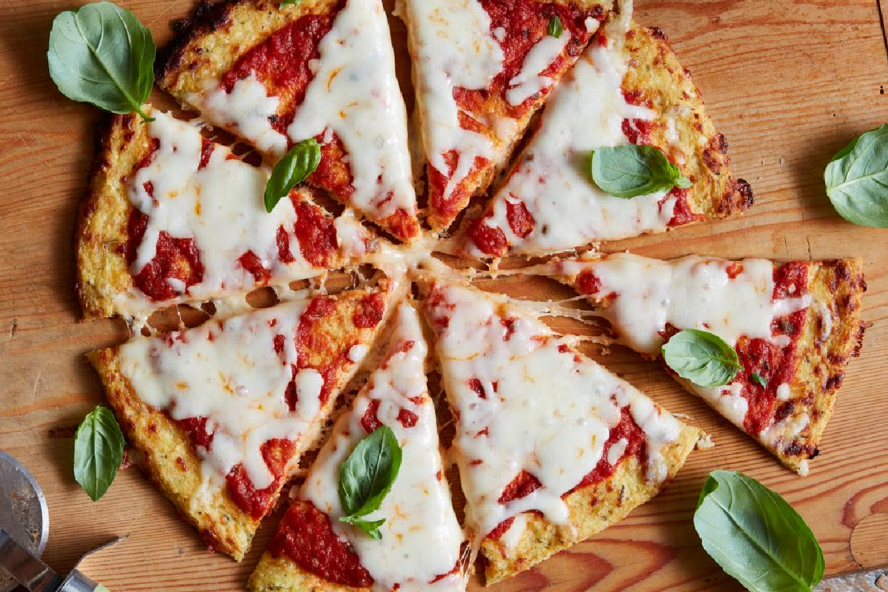 An overhead shot of a cheese cauliflower pizza with fresh basil