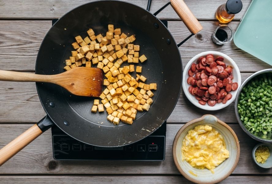 cooking cubes of tofu in black wok