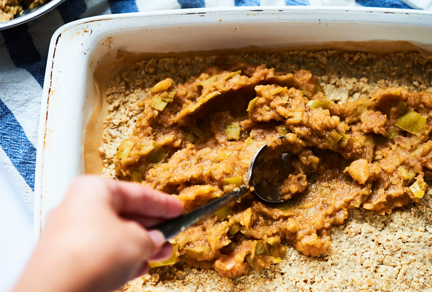 Apple mixture being spread over crust for apple pie squares