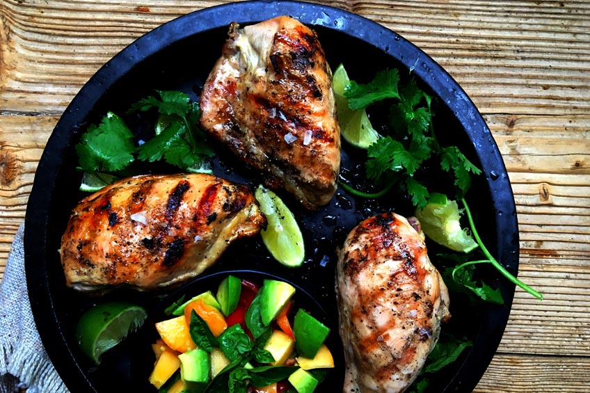 grilled honey lime chicken thighs on a bed of herbs with peach avocado salsa