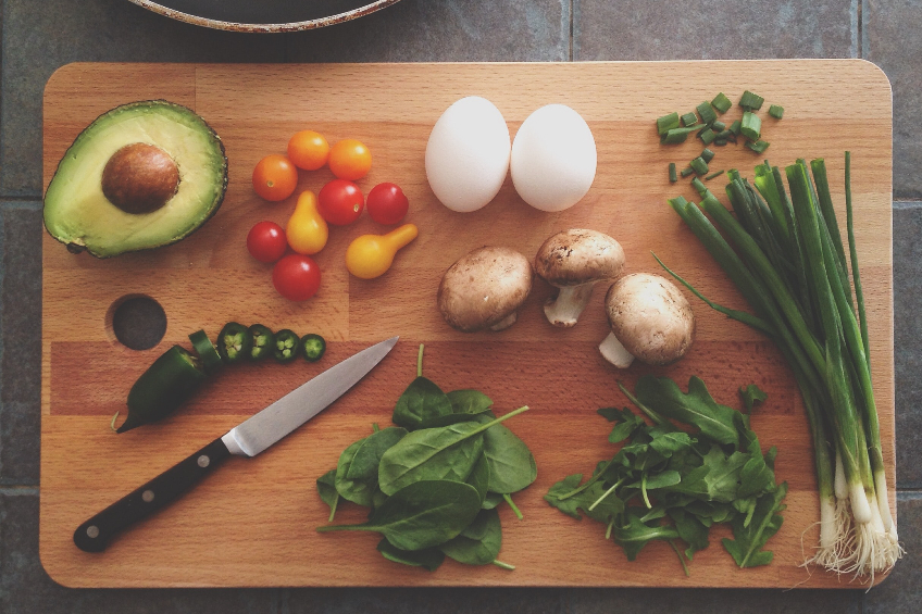 A wooden cutting board with a knife and various fresh produce on it