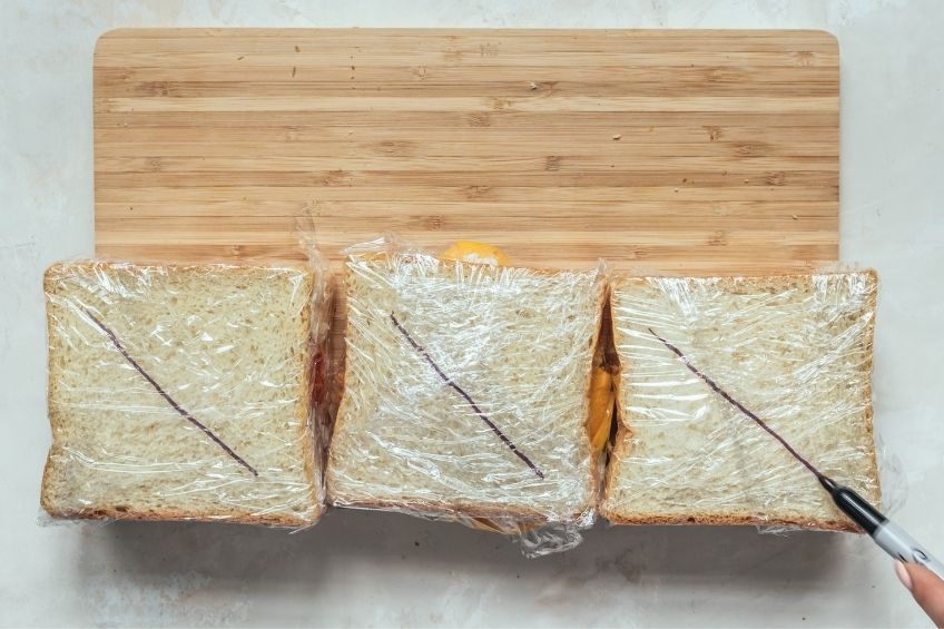 three Japanese fruit sandos with strawberries, mango and kiwis wrapped in plastic wrap