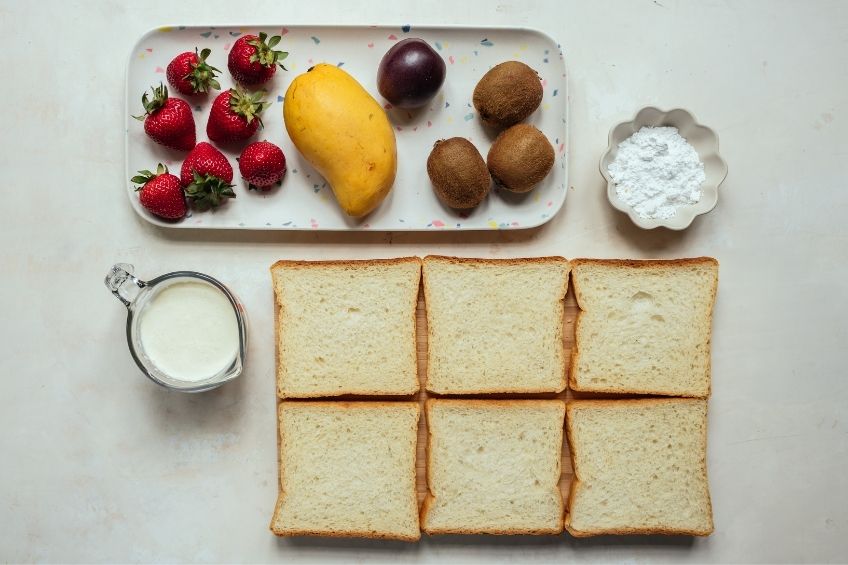 three Japanese fruit sandos with strawberries, mango and kiwis ingredients on countertop