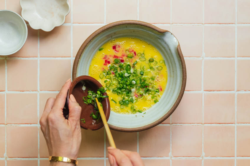 eggs, scallions and peppers being mixed together in a ceramic bowl