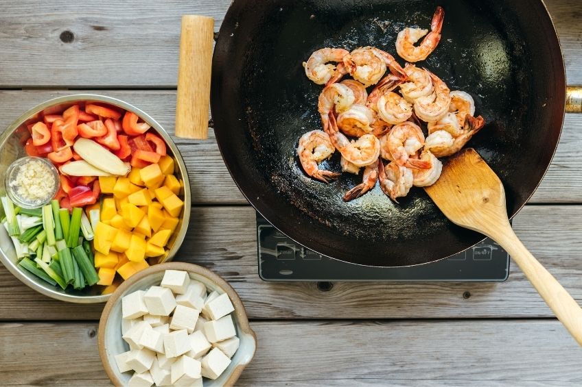 Sweet and sour shrimp and tofu being cooked in wok