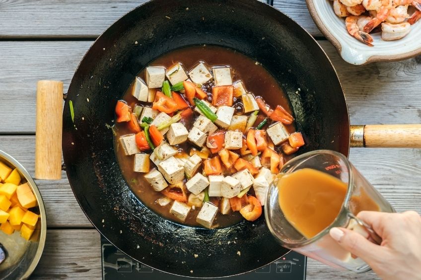 Sweet and sour shrimp and tofu being cooked in wok