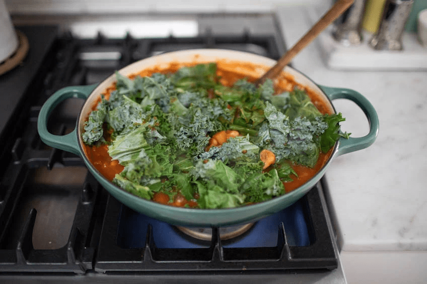 A pot on a stove with tomato sauce and kale