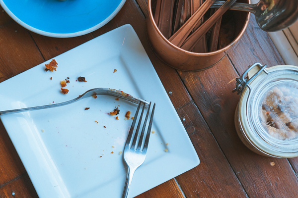 An empty white plate with a fork next to a container of utensils