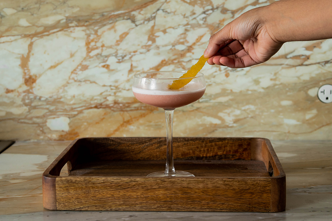 Abhi garnishing the Pink Lady cocktail with lemon peel