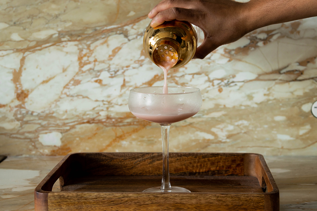 Abhi straining Pink Lady cocktail into a coupe glass