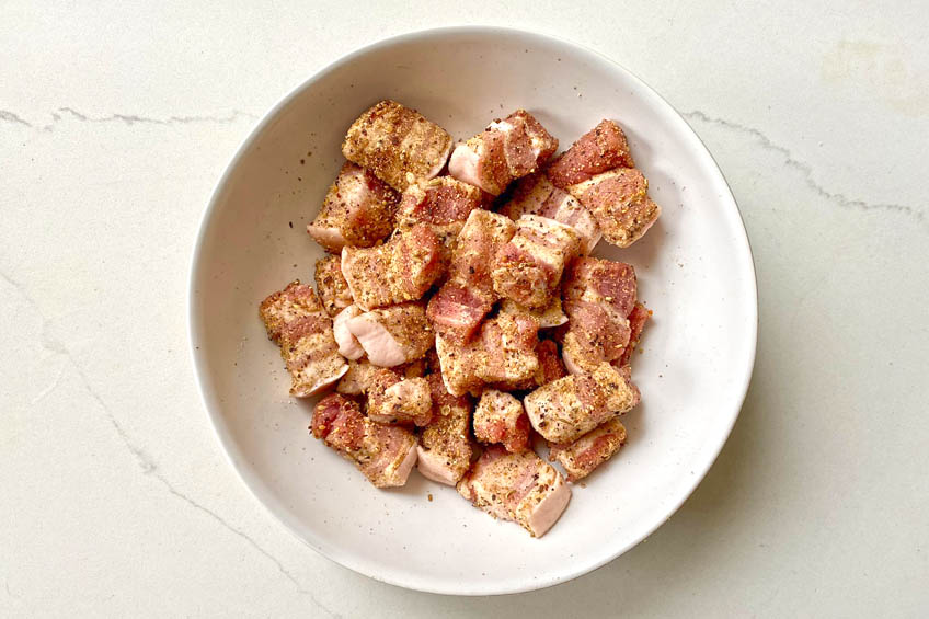 Pork belly tossed with spices in a bowl.