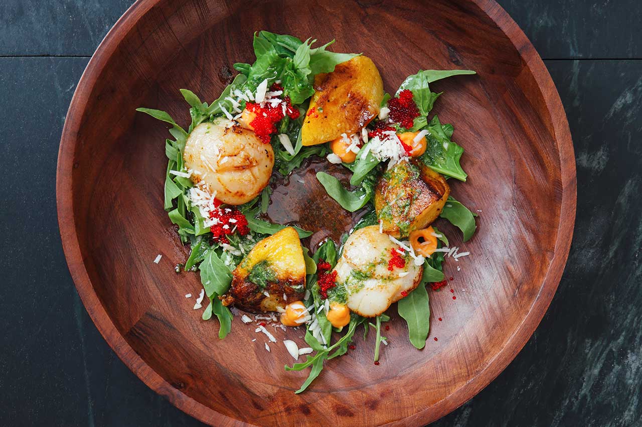 a bowl of salad greens with scallops and dressing