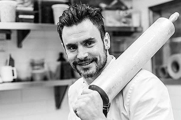 A black and white photo of Steve Hodge smiling and holding a metal rolling pin