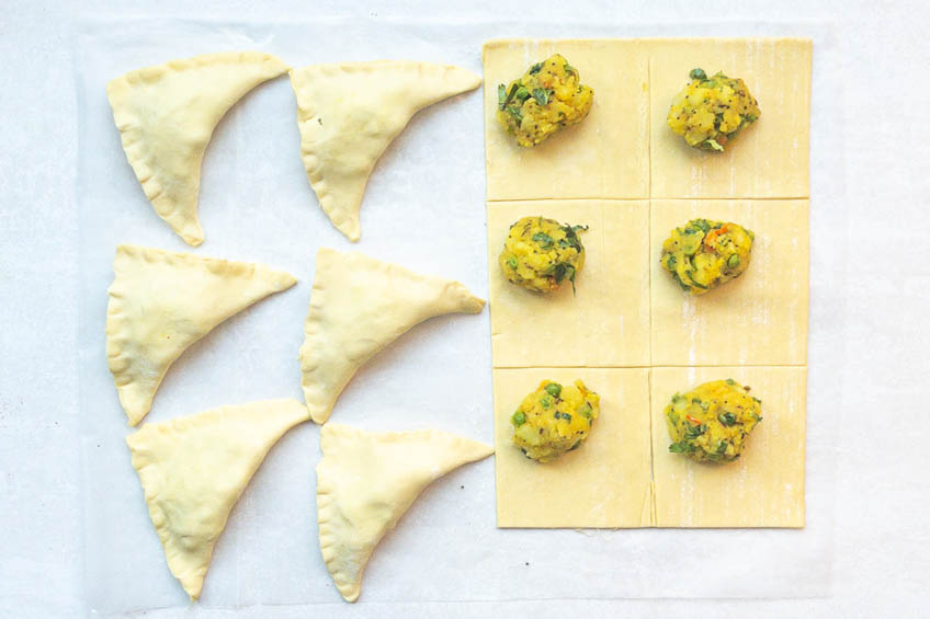 Folded and unfolded samosas on a baking tray