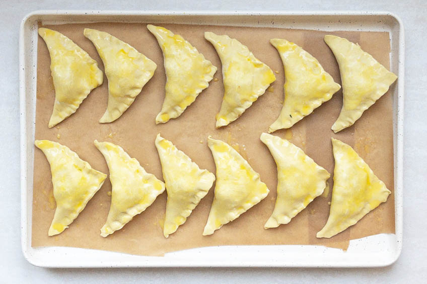 Samosas brushed with egg way on a baking tray