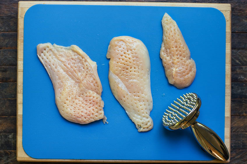 Chicken on a cutting board being pounded with a mallet