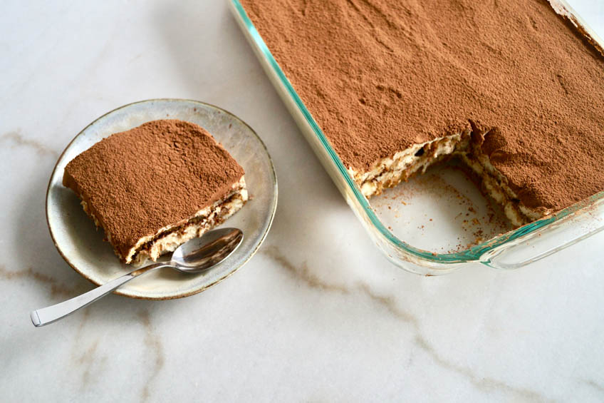 A slice of caramalized banana tiramisu beside tiramisu in a dish.