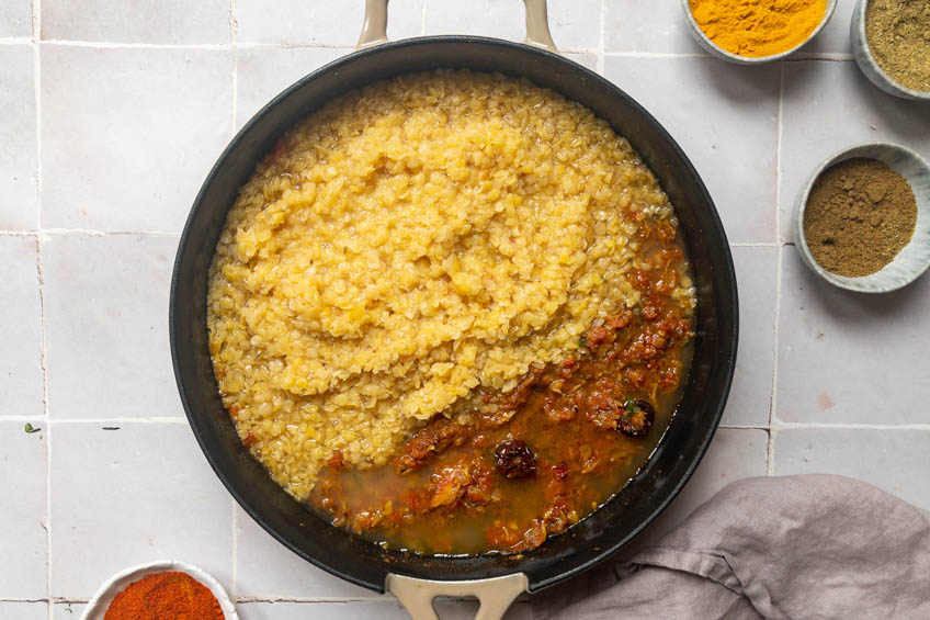 Cooked lentils being combined with tadka.