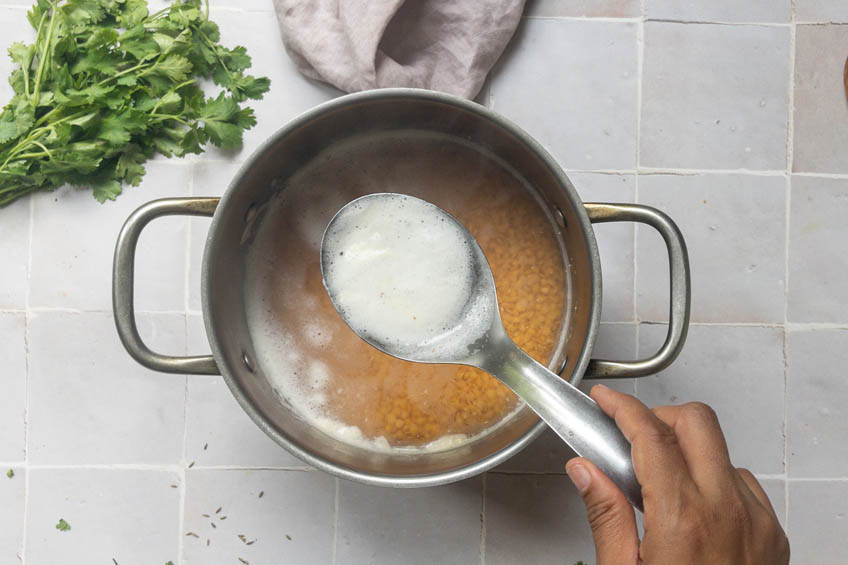 Scum being skimmed off of boiled lentils