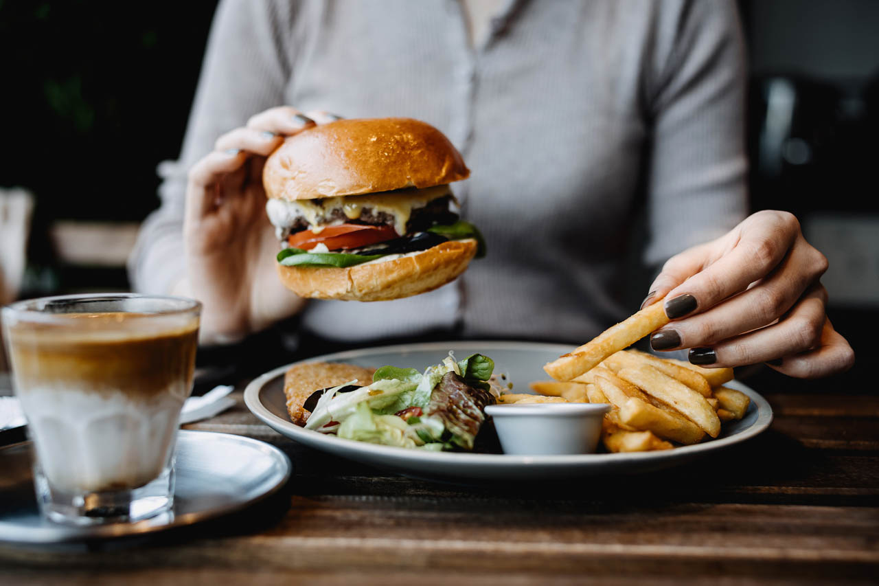 The hands of a woman eating a burger and fries alone.