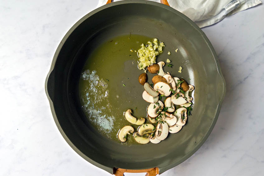 A frying pan with garlic, herbs and sliced mushrooms