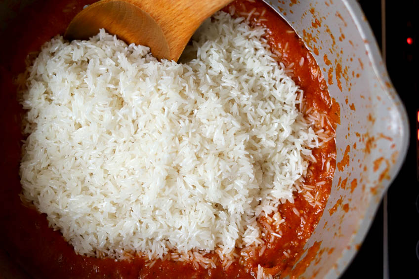 Rice being added to a pot of tomato stew for jollof rice