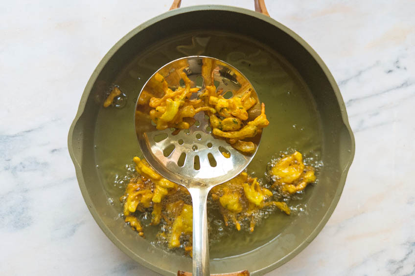 Onion pakora being fried in a pan