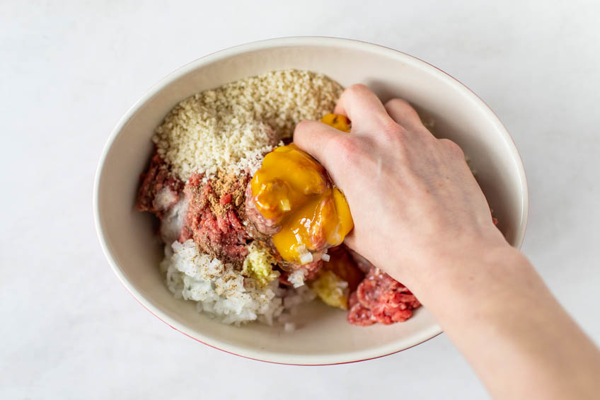 Ingredients for air fryer meatballs being mixed by hand in a bowl