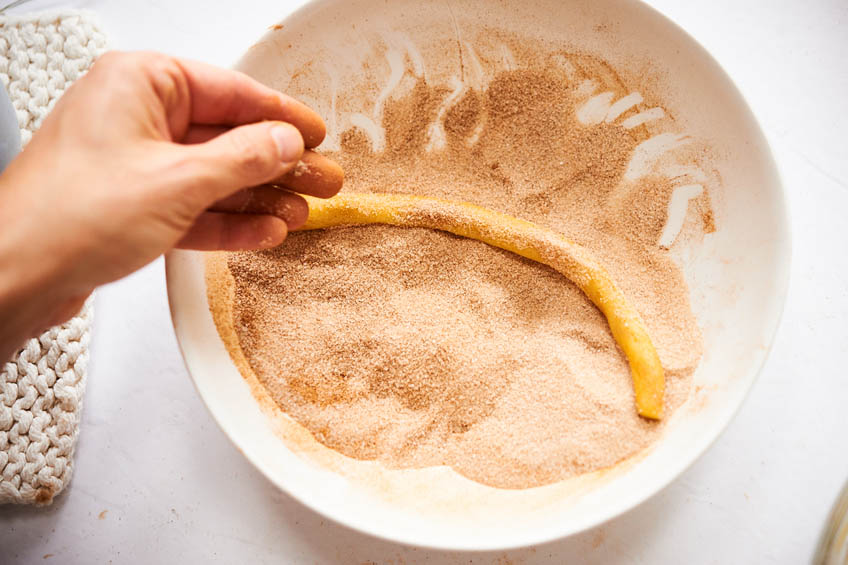 Dough for cinnamon twist cookies being rolled in cinnamon sugar