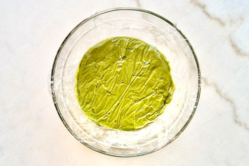 Matcha cookie batter in a bowl covered with plastic wrap