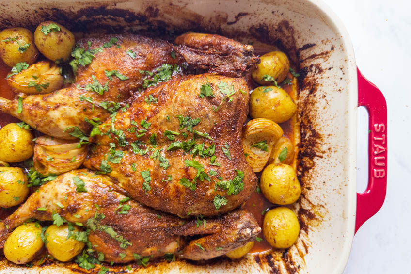 Whole roasted tandoori chicken with potatoes in a casserole dish