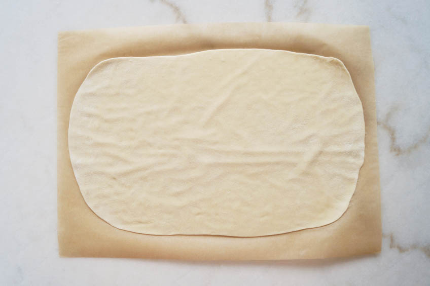 Flammkuchen dough on a sheet of parchment paper