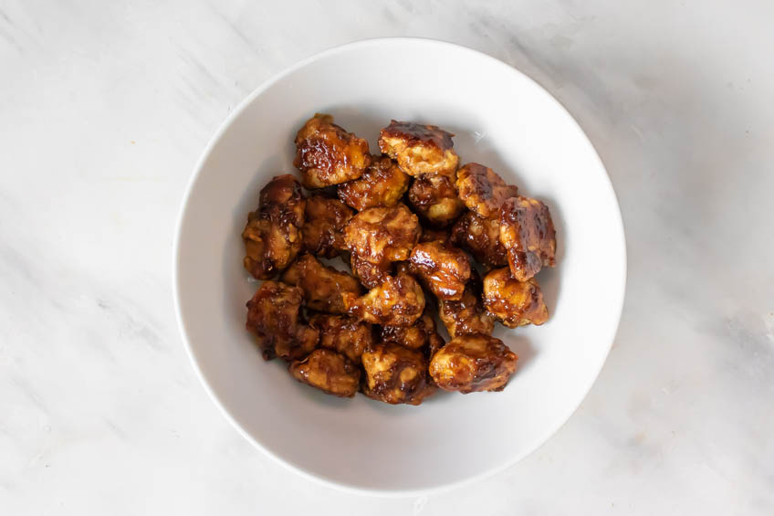 Chicken bites tossed in honey garlic sauce in a bowl.