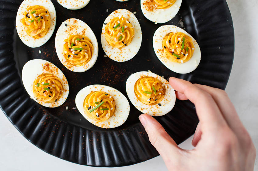 A hand picking up a honey-sriracha devilled egg