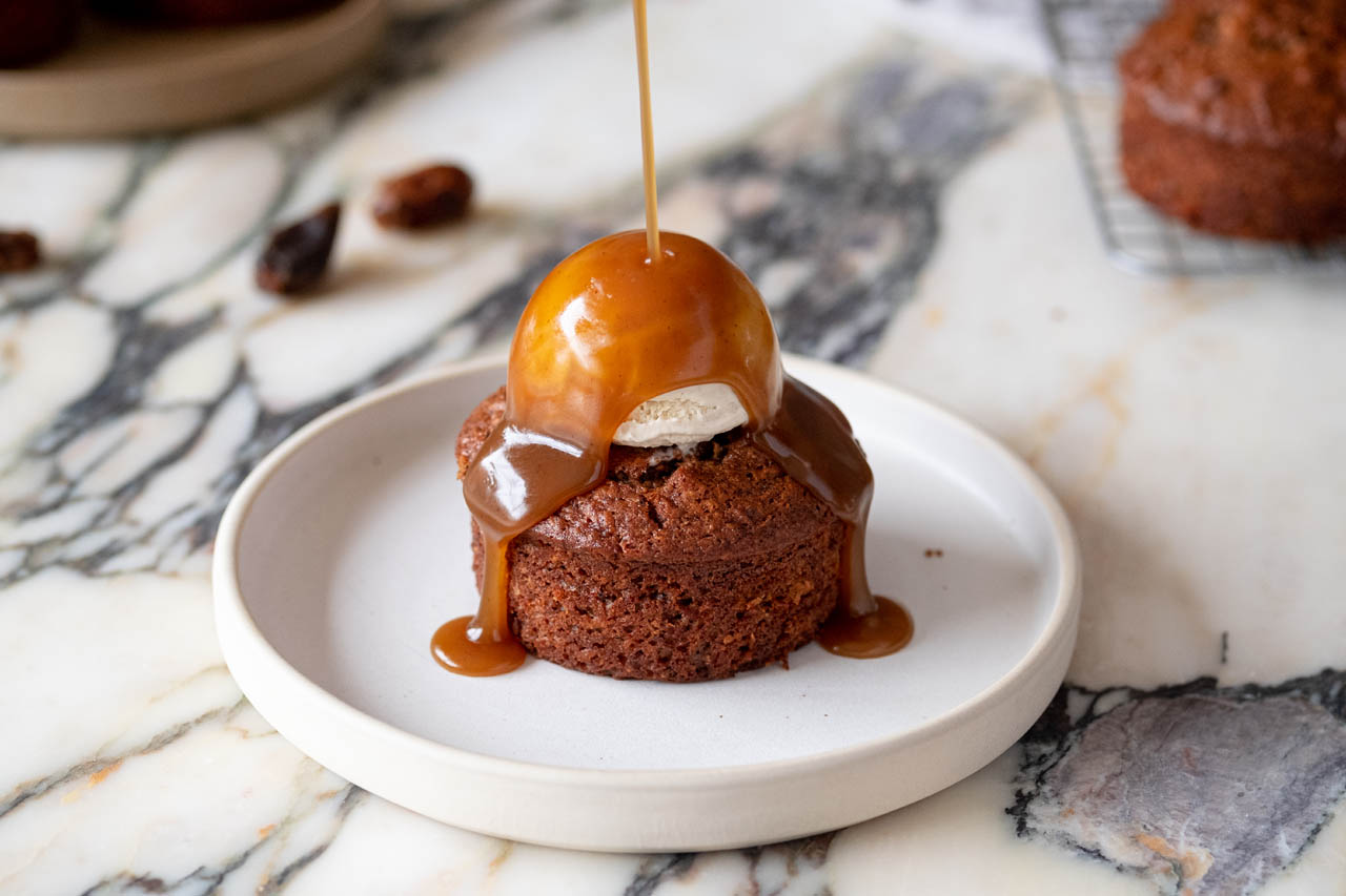 Sticky toffee carrot cake being topped with toffee drizzle