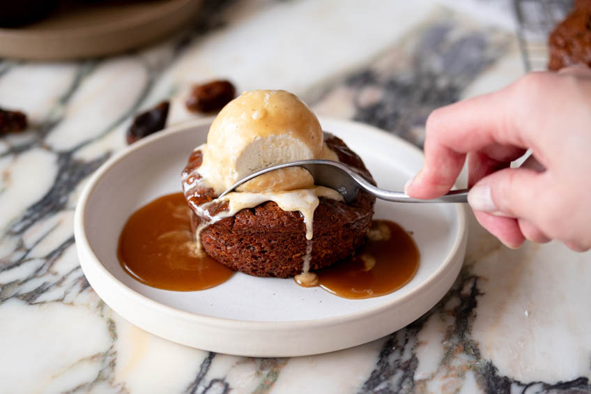 A bite being taken out of sticky toffee carrot cake topped with ice cream.