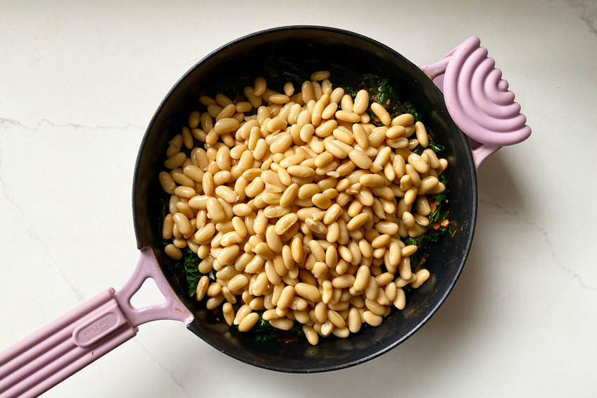 Beans on top of wilted kale in a skillet.