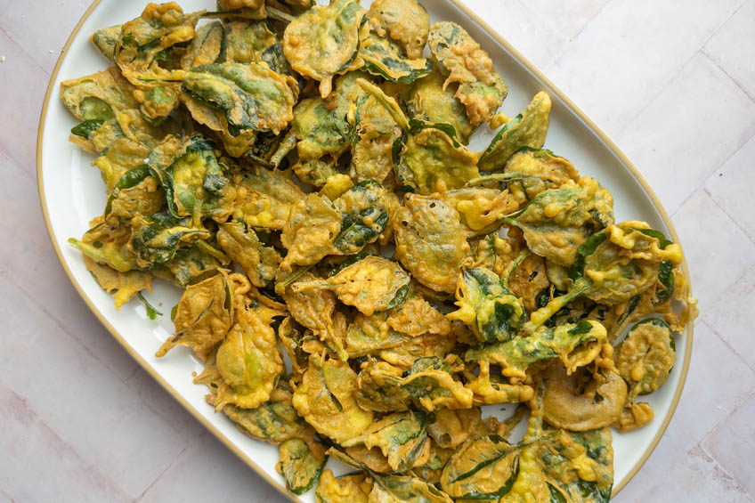 Fried spinach pakora chaat on a paper towel-lined plate.