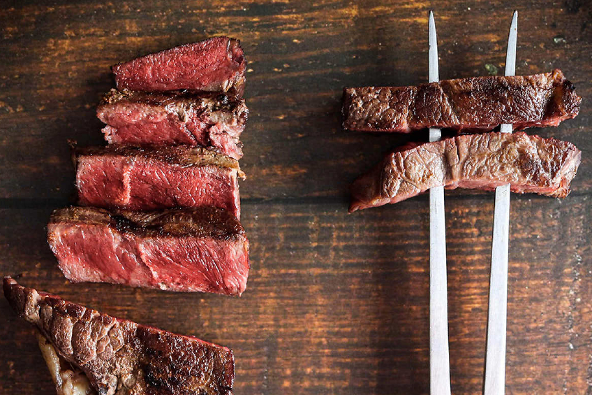 A shot of a ribeye steak, cooked to a perfect medium rare, cut up on a wooden board