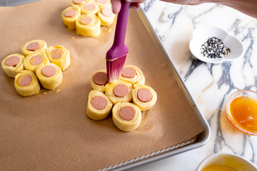 Unbaked Chinese Hotdog Flower Buns being brushed with egg wash