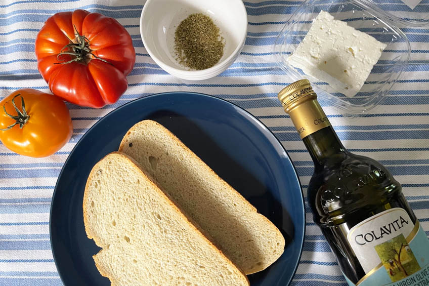 A blue plate with two slices of bread, with an heirloom tomato and olive oil nearby