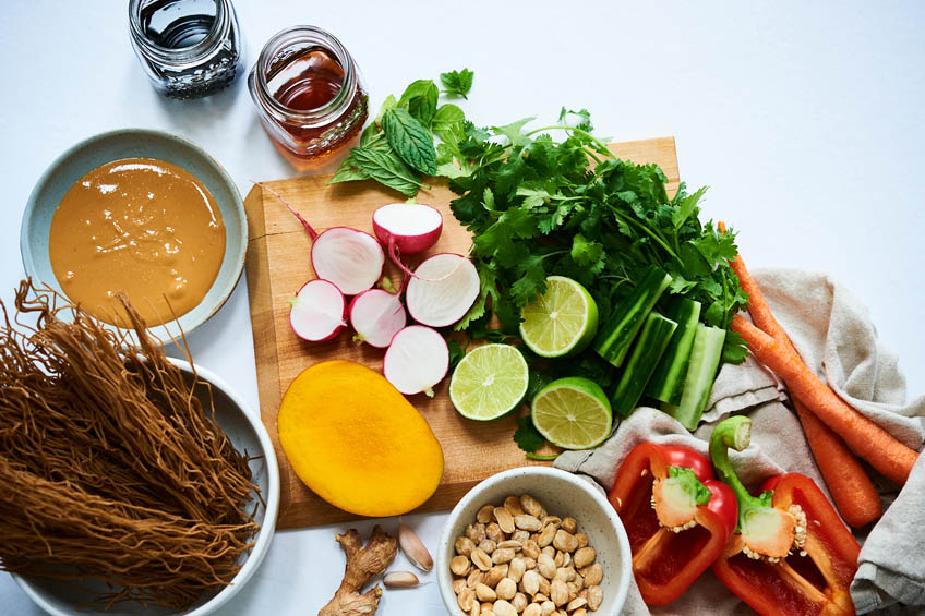 A flat lay of the ingredients needed for a cold noodle salad: veggies, soba noodles, peanut butter, soy sauce and honey