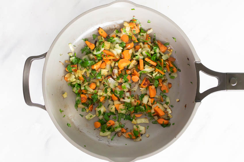 A frying pan with onion, carrots and fresh herbs