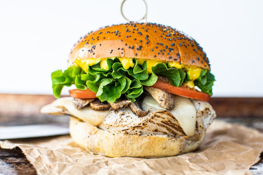 A chicken and Swiss cheese burger on a poppyseed bun with mushrooms, lettuce, tomatoes and mayo.