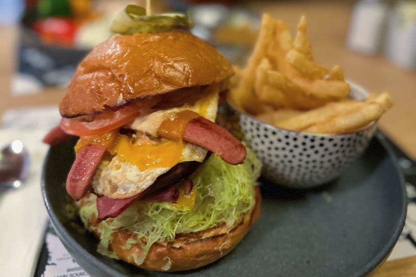 A burger topped withonions, lettuce, bacon, egg, aged Cheddar cheese, a wiener, tomato, and special sauce.