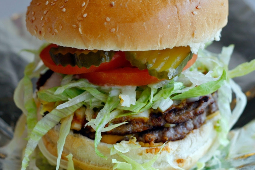 A burger made with a hand-pressed beef patty, freshly baked bun, cheese, chili, mustard, onions, pickles, lettuce, tomatoes and mayonnaise.