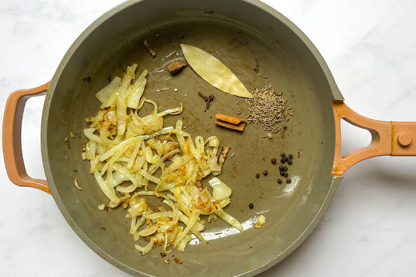 Sliced onions and whole spices in a saute pan