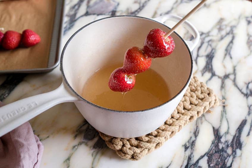 Strawberries being dipped in candy syrup