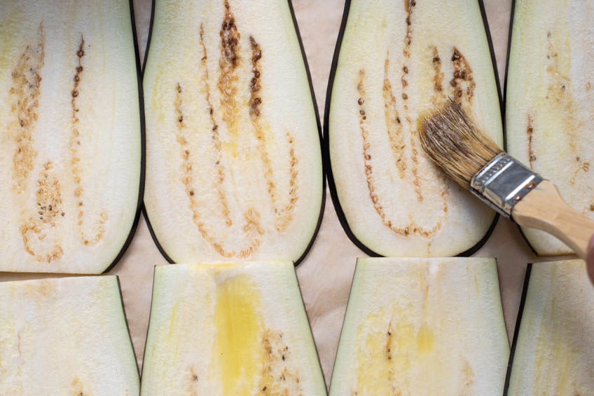 Thinly sliced eggplant being brushed with olive oil