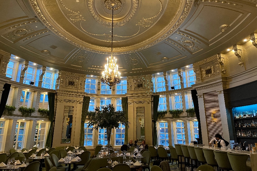 The interior of the Oval Room Brasserie at the Fort Garry Hotel in Winnipeg, Manitoba, featuring a chandelier, ornate ceiling and walls, and large windows.